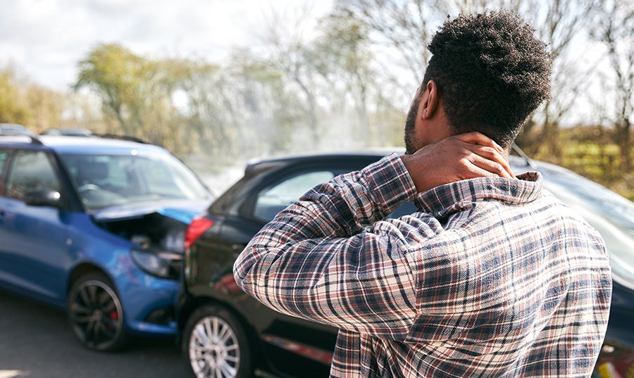 Man holding the back of his neck as he stands in front of a rear-end collision